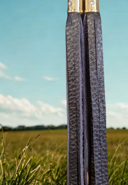 Deep mulberry handmade leather boot tassel in front of a meadow